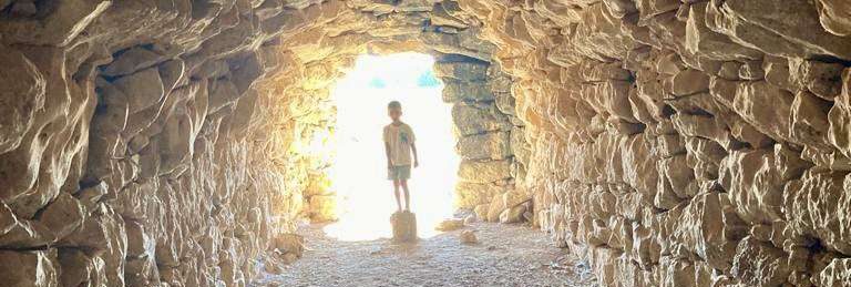 es la Barraca Grande de Casas Bajas, fotografiada desde el interior. Al fondo, en la salida, existe una silueta de niño, quien está de pie sobre una piedra. La figura del niño contrasta con la luminosidad del exterior