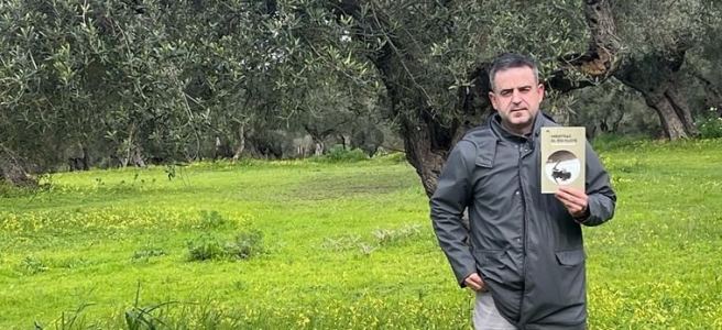 Delante de una campiña y olivo andaluces, Blas Valentín muestra su libro.