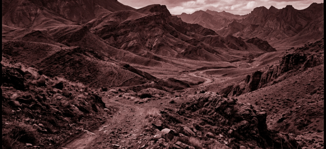 Rocky dirt road leading through rough mountainous landscape with cloudy sky