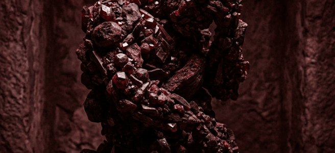 Dark red crystalline sculpture with irregular cluster shape on stone pedestal