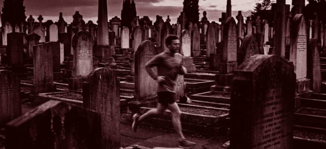 Man running through cemetery with numerous gravestones at dusk